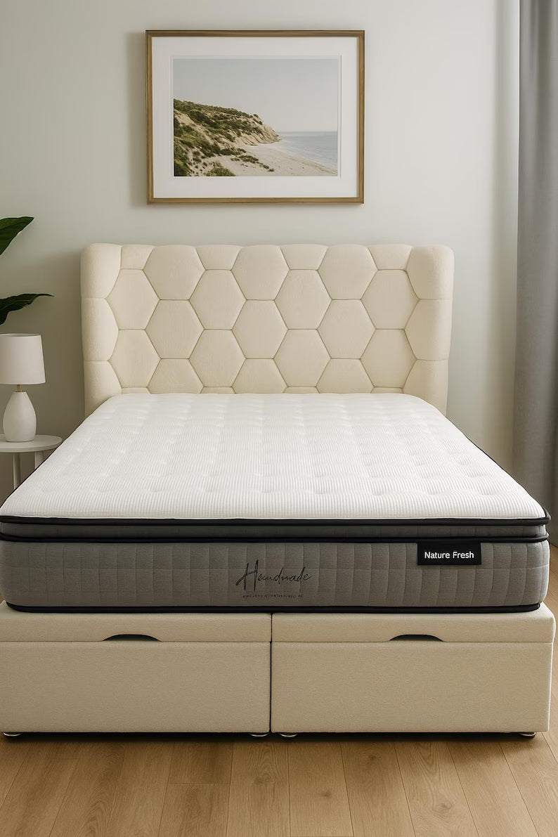 Beige mattress with quilted headboard in a room setting with a lamp and framed picture on the wall.